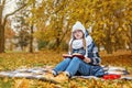 teen girl in a cold park studying a book and sitting on a blanket on a cold ground