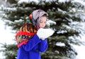 Teen girl in colored shawl, white mittens blowing snowflakes from her hands on background of snow and forest.