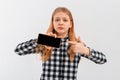 Teen girl with concerned face pointing at mobile phone, looks worried at camera, showing something upsetting on smartphone. Indoor Royalty Free Stock Photo