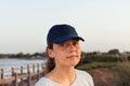 Teen girl in dark blue baseball cap standing by the sea at sunset. Cap mockup