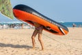 Teen girl drags on her back a large inflatable boat on a sandy beach