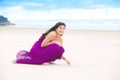 Teen girl in dress kneeling, writing in sand on beach