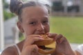 Teen girl eating hamburgerand laughing on the balcony on a sunny day Royalty Free Stock Photo