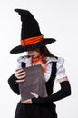Teen Girl In Halloween Witch Costume And Black Hat Holding Large Vintage Book, Studio Portrait On White Background