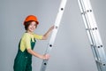 teen girl laborer in protective helmet and uniform on ladder, building