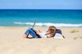 A teen girl lies on the beach with a laptop