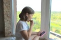 Teen girl listens to music on the phone by the window. Royalty Free Stock Photo