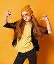 Cool teen girl with long red hair in knitted hat, yellow glasses and t-shirt is pointing fingers thumbs at herself