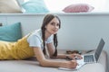 teen girl lying on sofa with laptop textbook smartphone earphones