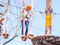 Teen girl in orange helmet climbing in trees in forest adventure park
