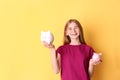 Teen girl with piggy banks on color background