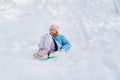 A teen girl in a blue coat tries to move on a sledge from a snow slide