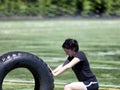 Teen girl pushing heavy old tire on sports field during hot day