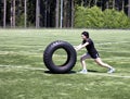 Teen girl pushing heavy tire on sports field during hot day