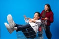 Teen girl pushing her teenage boyfriend in a shopping cart against blue background in studio Royalty Free Stock Photo