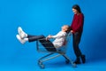 Teen girl pushing her teenage boyfriend in a shopping cart against blue background in studio Royalty Free Stock Photo