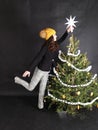 Teen girl putting white paper star on top of Christmas tree