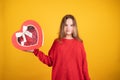 Teen girl in red sweater holding a red heart-shaped gift box in her hand on uellow background Royalty Free Stock Photo