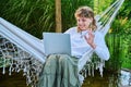 Teen girl relaxing in hammock using laptop for video communication, waving hand Royalty Free Stock Photo