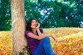 Teen girl sitting against autumn tree using cell phone Royalty Free Stock Photo