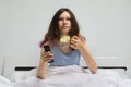 Teen girl sitting in bed with glass of water with lemon holding TV remote in hand Royalty Free Stock Photo