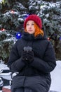 Teen girl sitting on bench in park against decorated fir tree in winter evening. Beautiful young woman wearing casual clothes Royalty Free Stock Photo