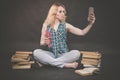 Teen girl sitting on the floor next to books, does not want to learn, drinking juice and taking a selfie on the smartphone