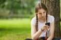 Teen girl sitting near tree with mobile phone Royalty Free Stock Photo