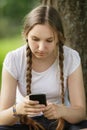 Teen girl sitting near tree with mobile phone Royalty Free Stock Photo