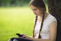 Teen girl sitting near tree with mobile phone Royalty Free Stock Photo