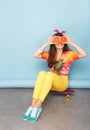 Happy girl holding grapefruit on her eyes, seated on skateboard, posing in studio, over blue background. Copy space. Royalty Free Stock Photo