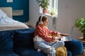 Teen girl studying online listening online class in headphones on laptop sitting on sofa. Royalty Free Stock Photo