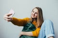 Teen girl takes selfie on cellphone and smiles at camera. Beautiful girl in yellow sweater and blue jeans holding mobile phone and