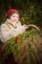 Teen girl in thick coat and a red sash with basket of fir branches and berries in cold winter day in forest. Medieval