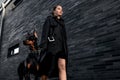 Teen girl walking down the street with her doberman. Great view. Full length of a beautiful young girl in a black cloak. Security Royalty Free Stock Photo