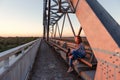 Teen girl wanderer sitting on steel bridge design in docks and looking away at sunset Royalty Free Stock Photo