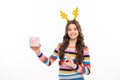 Teen girl wear winter sweater and deer antlers, hold gift celebrating christmas holidays on white studio background Royalty Free Stock Photo