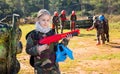 Teen girl wearing uniform and holding gun ready for playing with friends on paintball outdoor