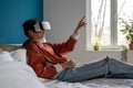 Teenage girl wearing virtual reality headset lying on bed at home exploring metaverse. VR concept