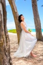 Teen girl in white dress by tree along Hawaiian beach Royalty Free Stock Photo