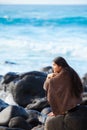 Teen girl wrapped in towel sitting on rocky beach