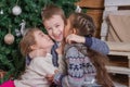 Teen girls kissing brother under Christmas tree, everybody laugh Royalty Free Stock Photo