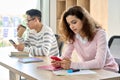 Teen Hispanic girl and Asian guy sitting using cell mobile phones in classroom. Royalty Free Stock Photo