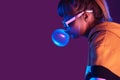 Teen girl wear stylish sunglasses hoodie blow bubble gum on purple background Royalty Free Stock Photo