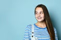 Teen lady in jeans overall and striped sweatshirt. She smiling, looking aside, posing against blue background. Close up