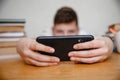 A teen looks into a black smartphone holding it at arm's length at home at a table among textbooks. Smartphone in focus
