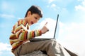 Teen pointing up while playing a laptop outside