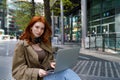 Teen redhead hipster girl using laptop on city urban street outdoors. Royalty Free Stock Photo