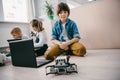 teen schoolboy with laptop and robot sitting on floor