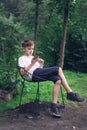 Teen sits on chair outdoors and looking at phone. Vertical frame